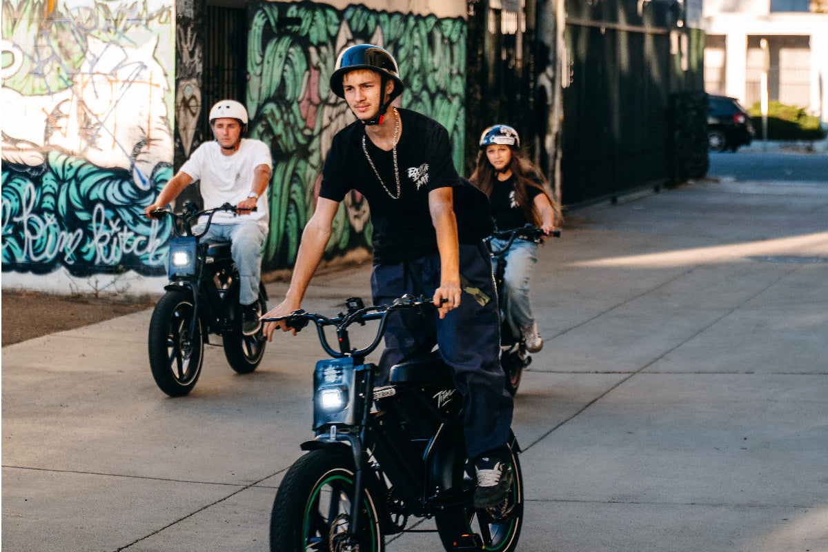 Three helmeted riders riding Heybike Titan electric bikes together on an urban street with colorful graffiti walls.