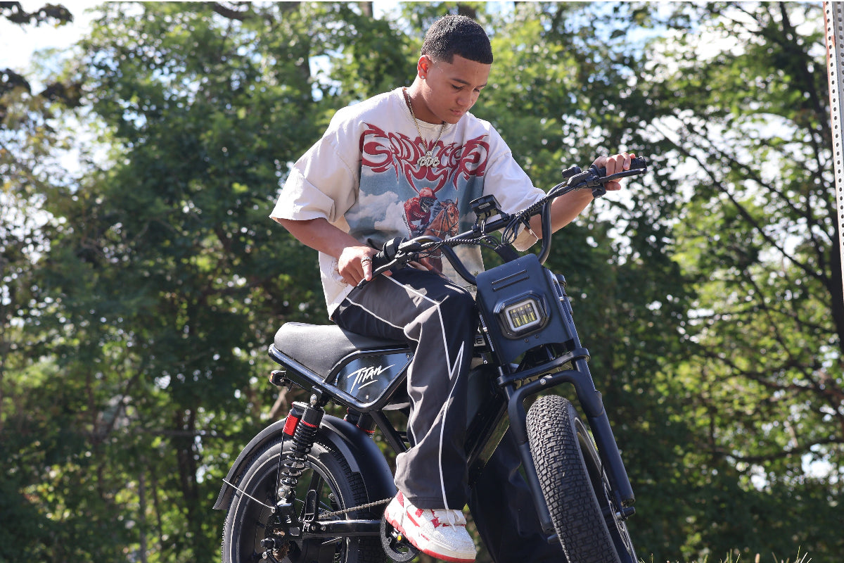 A rider in a white T-shirt sits on a black Heybike Titan electric bike outdoors, looking down at the handlebars.