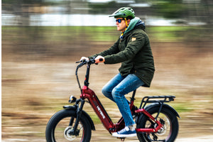 A rider wearing a green helmet rides a red Heybike folding fat-tire electric bike along an outdoor trail.