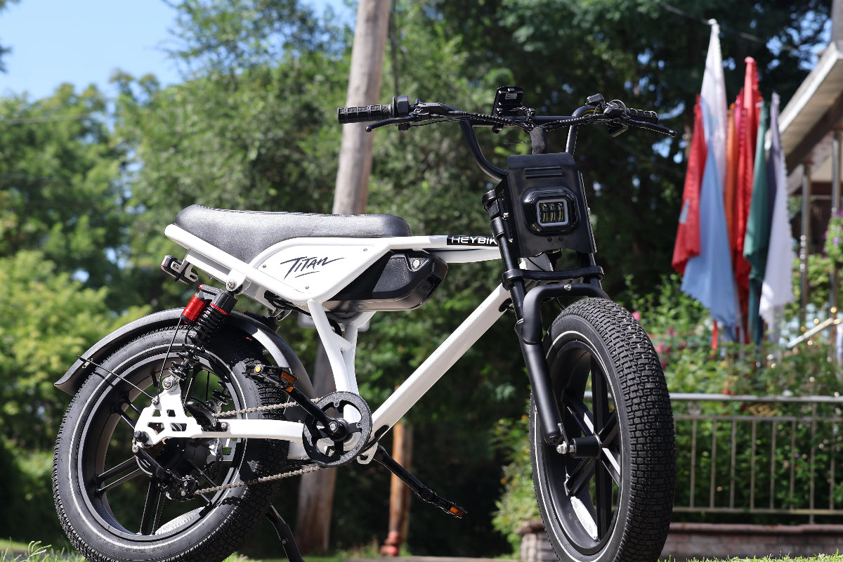 White Heybike fat-tire electric bike parked outdoors with trees and flags in the background.